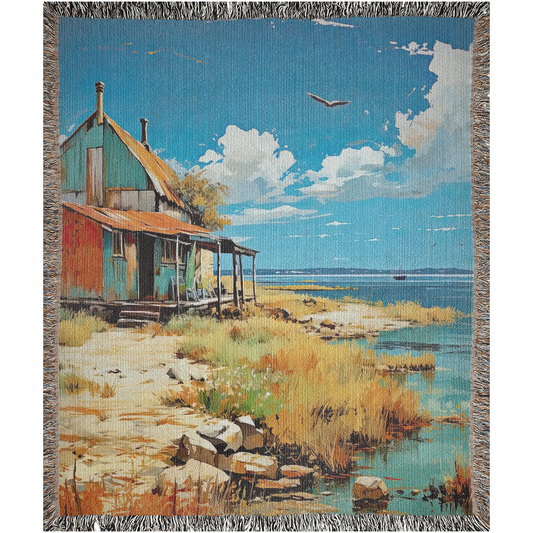 Oléron Shanty Woven Blanket featuring a house by the shore, showcasing intricate craftsmanship and made from 100% pure cotton for home décor.