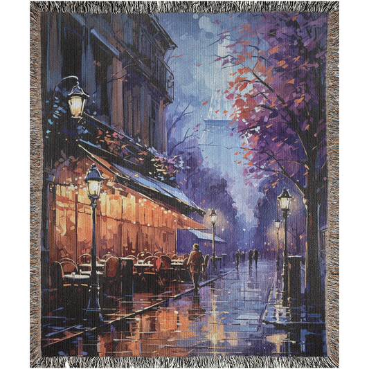 Paris in Lavender I Woven Blanket depicts a small street in Paris lined with tables and a cafe in the evening, highlighting an intricate design, embodying luxury and personal style. Crafted from 100% pure cotton.